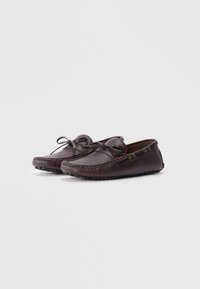 Zapatos de estilo mocasín de cuero marrón con punta redondeada, costuras en contraste y cierre con cordones. Suela de goma texturizada para mejorar el agarre.