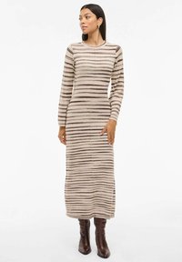 Langermet, tettsittende strikkekjole i beige med brune horisontale striper, med rund hals og strukturert stoff. Brukt med brune høye støvler.