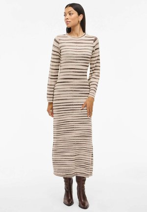 Pitkähihaisia, istuvia neulemekko beigen sävyssä, jossa on ruskeita vaakaraitoja. Mekossa on pyöreä kaula-aukko ja teksturoitu kangas. Yhdistetty polven ylle ulottuviin ruskeisiin saappaisiin.