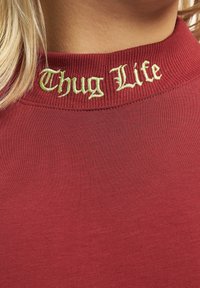 Rød bomull t-skjorte med ribbet krage, prydet med gult-grønn gotisk stil broderi av teksten "Thug Life."
