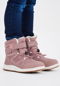 Rosa wasserdichte Stiefel mit weicher, flauschiger Fütterung, verstellbaren Riemen und strukturiertem Obermaterial. Gummisohle mit Profil für bessere Haftung.