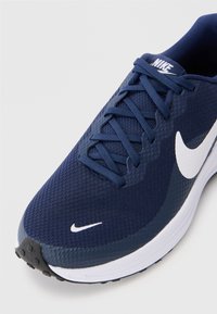 Ναυτικό μπλε αθλητικό παπούτσι με υφασμάτινη επικάλυψη από υφή, λευκό σήμα Nike, και αντίθετη λευκή σόλα. Διαθέτει παραδοσιακά κορδόνια και καουτσουκένια σόλα.