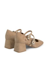 Beige suède blokhak schoenen met een spitse neus, voorzien van twee decoratieve strassaccenten en kruislingse banden over de voet.