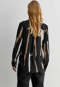 Czarna bluzka w pionowe paski w odcieniach beżu, bieli i jasnego brązu. Posiada długie rękawy i gładką teksturę materiału.