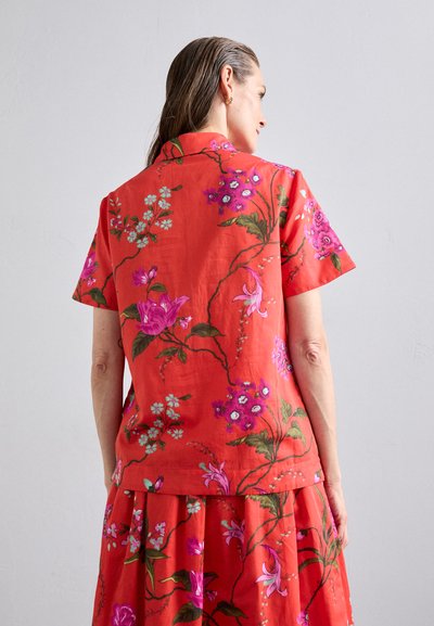 Short-sleeve red floral blouse features vibrant pink and green floral patterns with a relaxed fit and collared neckline.
