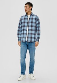 Camicia di flanella a quadri blu e neri, con colletto bottone, abbinata a jeans azzurri e sneakers bianche. Tessuto di morbida consistenza.