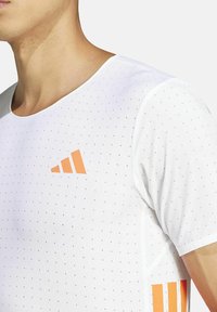 Weißes, kurzärmeliges Sportshirt mit glatter Textur, kleinen Perforationen und orangefarbenen Streifenakzenten auf der linken Brust und den Ärmeln.