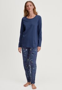 Marineblauw longsleeve shirt met een ronde hals, gecombineerd met pyjamabroek met patronen die verschillende vormen en kleuren op een donkere achtergrond tonen.