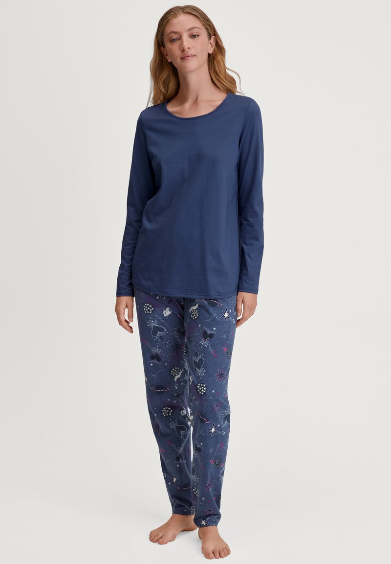 Marineblauw longsleeve shirt met een ronde hals, gecombineerd met pyjamabroek met patronen die verschillende vormen en kleuren op een donkere achtergrond tonen.