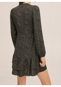 Černé šaty s malým bílým a béžovým květinovým vzorem, dlouhými rukávy, přiléhavým tělem a volánkovým lemem. Hladká látka s mírným leskem.