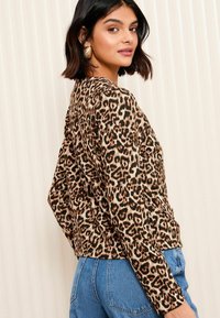 Il top a maniche lunghe con stampa leopardata presenta un tessuto morbido, una vestibilità comoda, un collo rotondo ed è abbinato a jeans a vita alta di colore azzurro chiaro.
