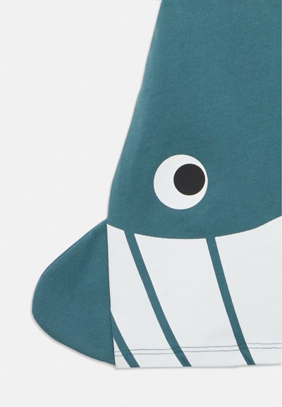 Tissu bleu avec un grand œil de dessin animé blanc et noir et un motif rayé noir et blanc ressemblant à une nageoire caudale de baleine ou de poisson.