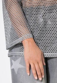 Top in rete grigio con un design morbido, caratterizzato da un motivo a nido d'ape e bordi a scallop. Abbinato a jeans grigi con un motivo a stelle.