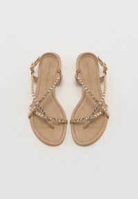Tan sandaler med flat såle, med kryssende stropper dekorert med klare og reflekterende steiner. Spenne lukking på siden.