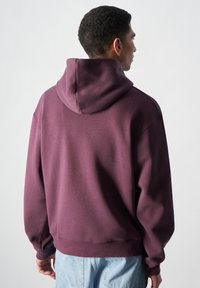 Sudadera morada con cordón, con un corte relajado, mangas largas y dobladillo acanalado. El material parece suave y tiene una textura lisa.