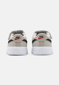 Nike sportcipő világosszürke velúr felsőrésszel, fekete csíkkal és fehér gumitalppal. A saroknál piros Nike logó található, valamint tépőzáras pánt.
