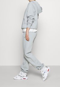 Ljusgrå hoodie och matchande sweatpants i mjukt tyg. Vit lager-på-lager-tröja under, kombinerad med vita och silverfärgade sneakers.