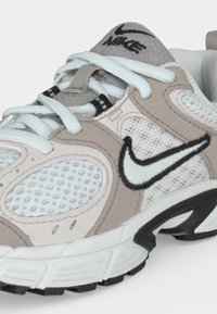 Μπεζ και λευκό παπούτσι για τρέξιμο Nike με ανοιχτό μπλε κορδόνια και μαύρο λογότυπο Swoosh σε διχτυωτό και σουέντ επάνω μέρος.