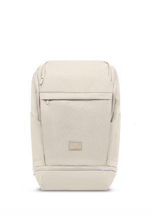 Mochila rectangular de color beige con bolsillo frontal con cremallera, bolsillos laterales y un pequeño parche con el logo de Johnny Urban en el panel frontal inferior.