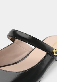 Μαύρο παπούτσι από δέρμα μπλίτζ με λεπτό λουρί, λεία υφή και χρυσά μεταλλικά στοιχεία. Διαθέτει στρογγυλή μύτη και μαλακό ροζ πάτο.