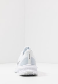 Bílé sportovní boty s šedými akcenty z pohledu zezadu, ukazujíc�í texturovanou podrážku a síťovinový svršek na bílém pozadí.