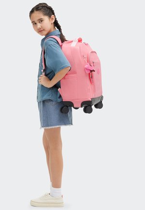 Zaino con ruote rosa, realizzato in un tessuto robusto, dalla superficie liscia e con una tasca laterale. Presenta ruote nere e un accessorio a charm da appendere.