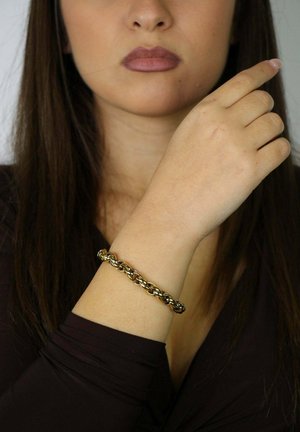 Pulsera de metal tono dorado con un diseño retorcido, que presenta eslabones redondeados que crean una apariencia texturizada. Llevada en una muñeca.