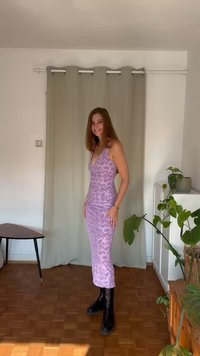 Μωβ φλοράλ φόρεμα με τιράντες σπαγγέτι; εφαρμοστή σιλουέτα; φορεμένο με μαύρες μπότες μέχρι το γόνατο; ξύλινο δάπεδο με ορατά φυτά εσωτερικού χώρου.