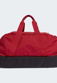 Bolsa de viaje de tela roja con dos asas gruesas, tapa con cremallera y un panel inferior negro; presenta una textura suave con costuras reforzadas.