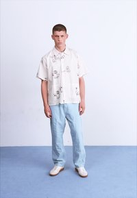Korte mouwen, crèmekleurig overhemd met zwarte abstracte prints, gecombineerd met lichtblauwe, losse broek en witte sneakers.