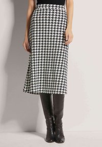 Schwarz-weißes Hahnentrittmuster-Midikleid mit ausgestelltem Saum, kombiniert mit kniehohen schwarzen Lederstiefeln. Glatte Textur des Stoffes, tailliert.