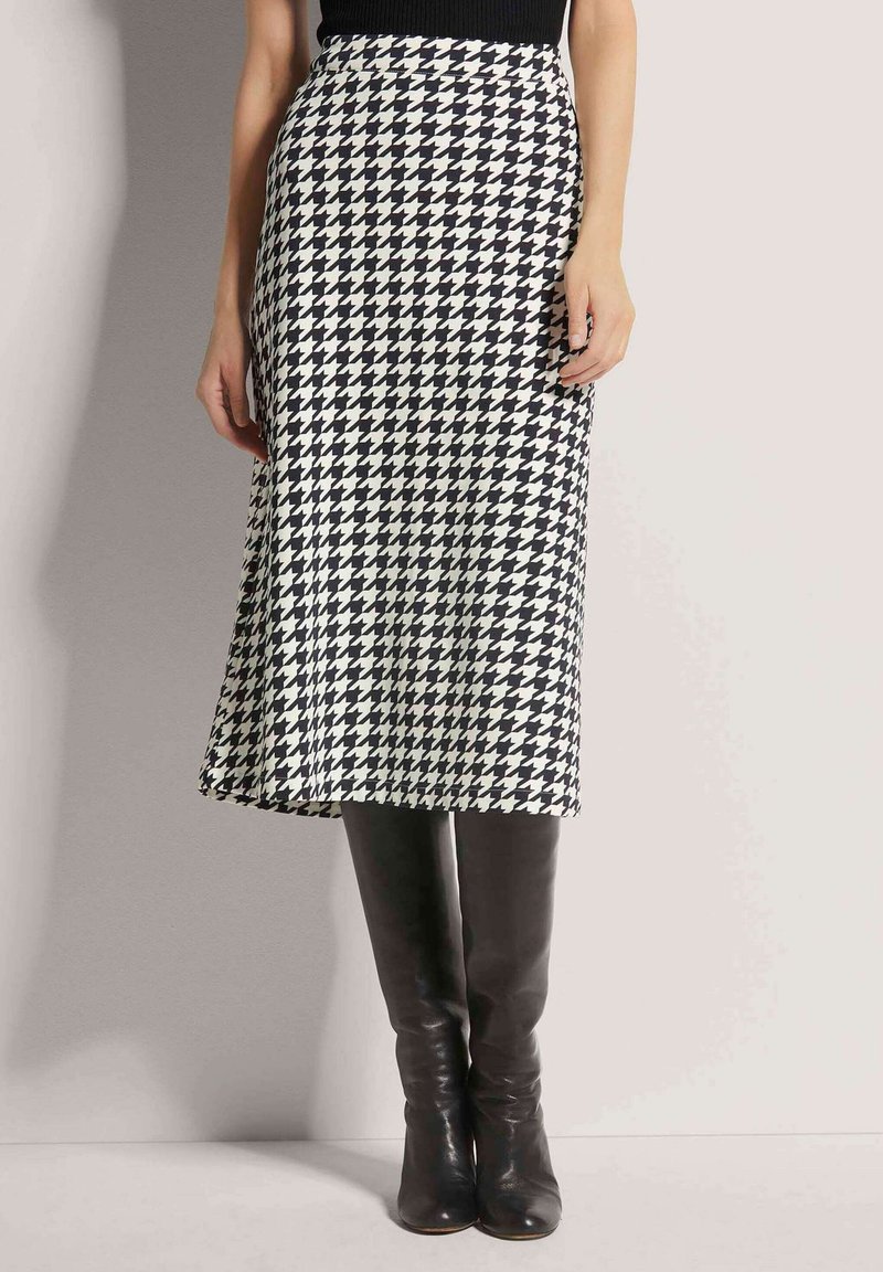 Schwarz-weißes Hahnentrittmuster-Midikleid mit ausgestelltem Saum, kombiniert mit kniehohen schwarzen Lederstiefeln. Glatte Textur des Stoffes, tailliert.