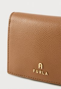 Brun tekstureret læderpung med guldfarvet hardware og præget "FURLA"-logo. Har syede kanter og en kompakt rektangulær form.