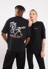 Black oversized t-shirts featuring a white horse graphic and red text on the back saying "BURNING SPIRIT" and "ETHERNAL SHADOW WISDOM."