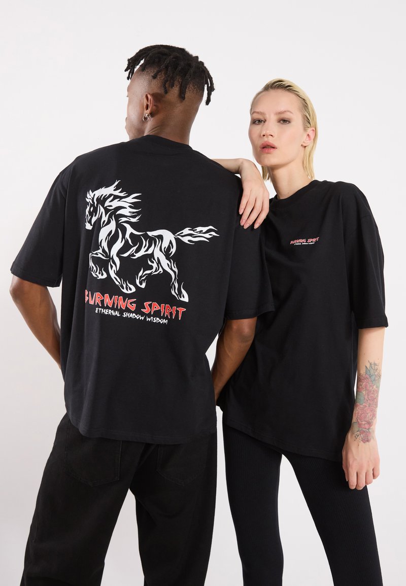 Black oversized t-shirts featuring a white horse graphic and red text on the back saying "BURNING SPIRIT" and "ETHERNAL SHADOW WISDOM."