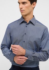 Camicia button-up in un motivo a spina di pesce blu, con colletto a punta, maniche lunghe con polsini abbottonati e taschino sul petto.