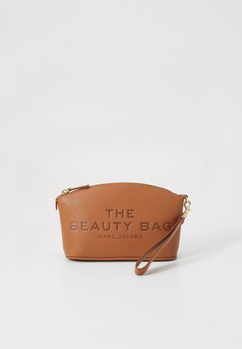 Bolso de muñeca texturizado marrón con cremallera dorada, etiquetado "THE BEAUTY BAG MARC JACOBS," sobre un fondo blanco.