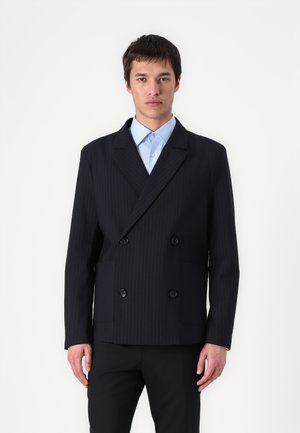 Doppelreihiger Blazer in Dunkelblau mit Nadelstreifen, ausgestattet mit einem Reverskragen, zwei Taschen und schwarzen Knöpfen, kombiniert mit einem hellblauen Hemd.
