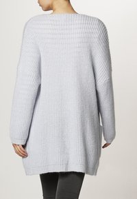 Langer, hellblauer Strickpullover mit langen Ärmeln, geripptem Muster und entspannter Passform. Verfügt über seitliche Schlitze am Saum für mehr Bewegungsfreiheit.