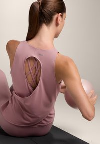 Light pink athletic tank top with a crisscross back design, paired with a pink ball. Smooth texture, fitted shape, and no visible logos.