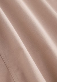 Tessuto beige morbido e liscio con trama a maglia fine e cuciture visibili lungo il bordo, mostrato in pieghe delicate.