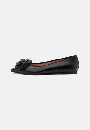 Schwarzer flacher Lederschuh mit spitzer Schuhspitze und dekorativer Blumenverzierung vorne, von der Seite gezeigt.