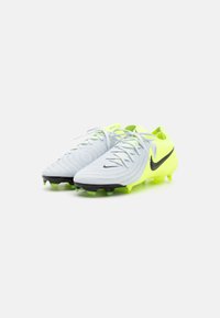 Piłkarskie korki Nike w jasnoszarym kolorze z teksturowanym wzorem, neonowymi żółtymi akcentami, czarnym logo Swoosh oraz czarnymi kołkami na podeszwie.