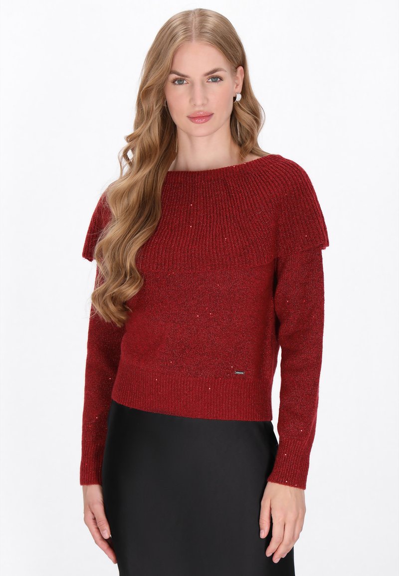 Pull en tricot rouge avec une texture côtelée, décolleté bateau et design superposé aux épaules, présentant un léger éclat sur l'ensemble.