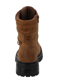 Brązowy zamszowy botek za kostkę z okrągłym noskiem, metalowym zapięciem na zamek, wyściełanym cholewą i grubą czarną gumową podeszwą. Posiada mały detal z logo.