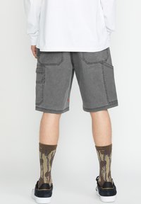 Graue Cargo-Shorts mit mehreren Taschen und kontrastierenden Nähten, kombiniert mit braun-beigen gemusterten Socken und schwarzen Sneakers.