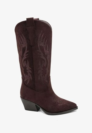 Botte de cowboy en daim marron avec un bout pointu, un talon carré et des motifs de flammes brodés le long de la tige. Dispose d'une languette pour faciliter l'enfilage.
