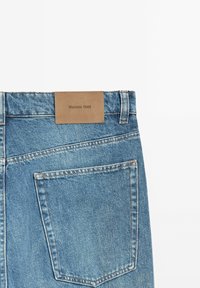 Jeans in denim azzurro chiaro con una toppa rettangolare in pelle marrone con la scritta "Massimo Dutti" impressa e una tasca sul retro con dettagli cuciti.