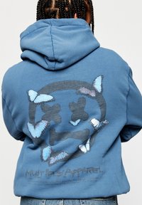 Blue hoodie featuring a graphic design with a circle and skull motif, surrounded by blue butterfly illustrations. Soft fabric with a relaxed fit.