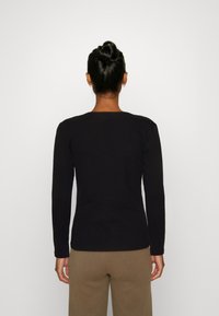 Schwarzes langärmliges Shirt mit Rundhalsausschnitt, taillierte Passform, aus weichem Stoff, getragen mit braunen Hosen. Keine sichtbaren Grafiken oder Muster.